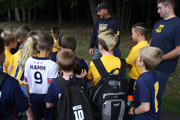 A group of players from multiple teams stand listening to the coaches
